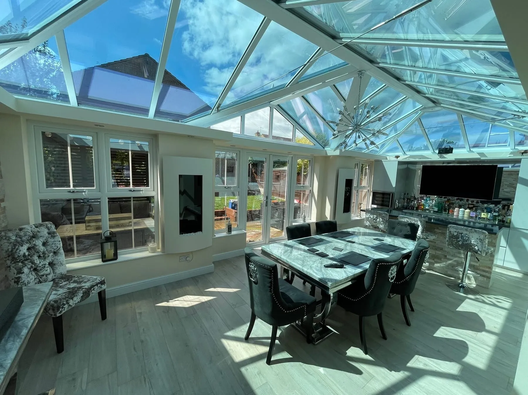 Inside a large conservatory, looking up through the clean glass roof over a dining table
