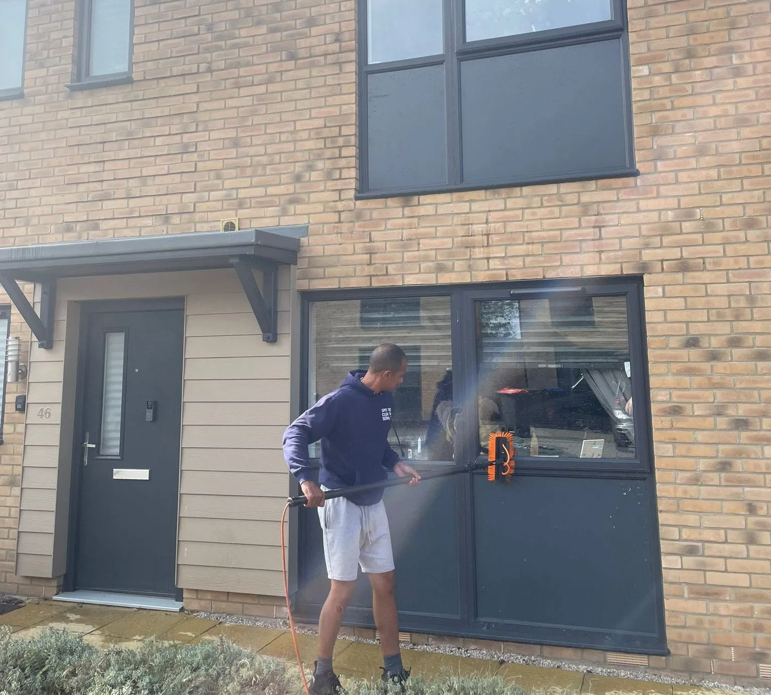 An operative cleaning a ground-floor window and front door with a water-fed pole