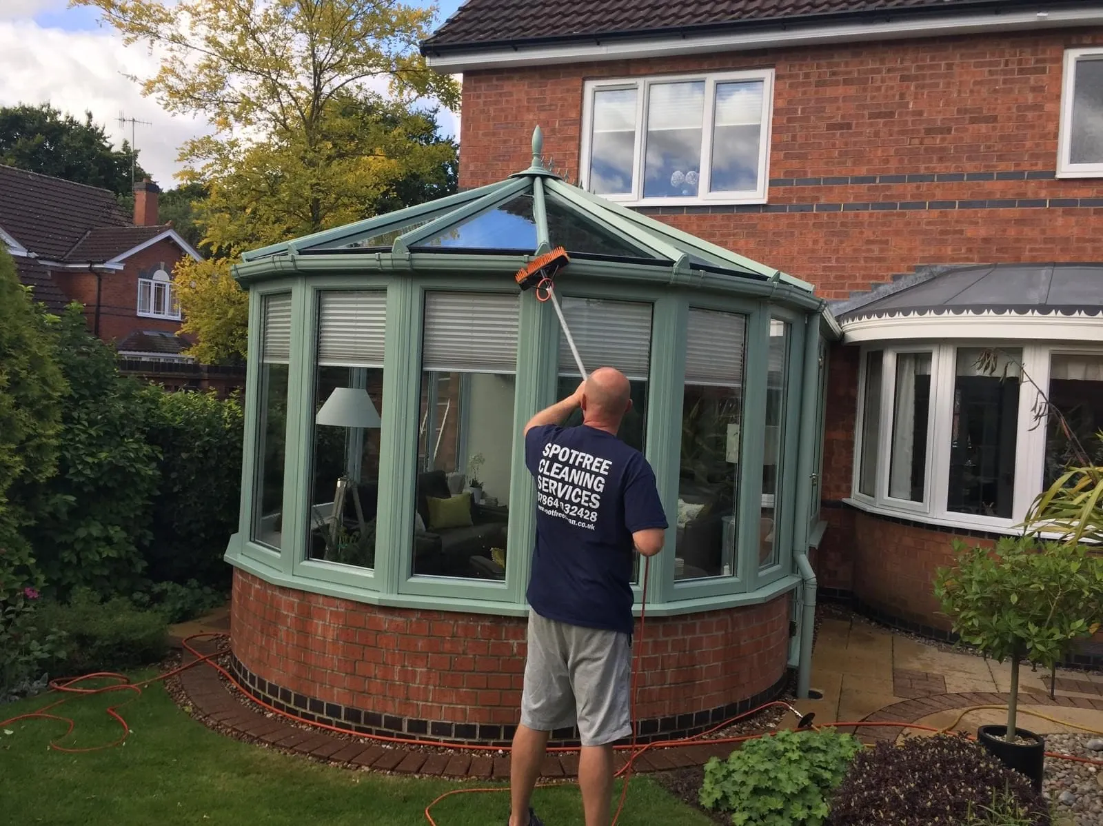 A SPOTFREE operative cleaning the windows of a green-framed conservatory with a water-fed pole