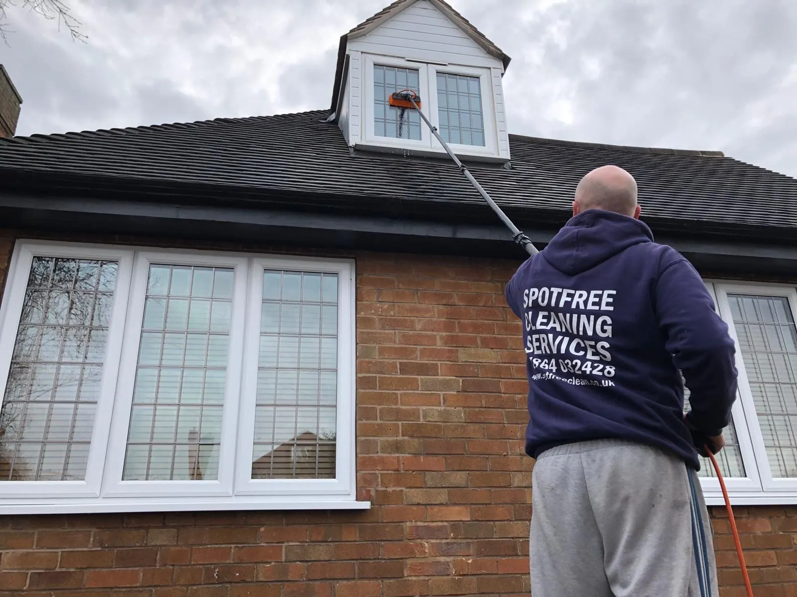 An operative cleaning the upstairs windows of a bungalow with a water-fed pole
